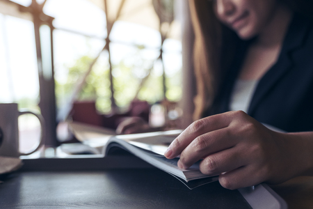 Closeup image of an asian businesswoman reading a book with coffee cup on table in cafe の写真素材