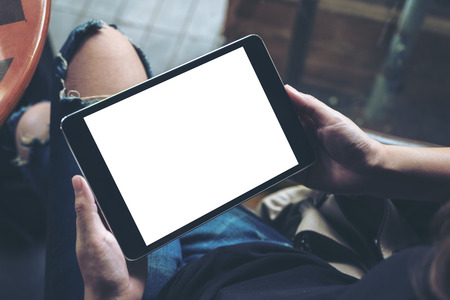 Mockup image of a woman sitting cross legged and holding black tablet pc with blank white desktop screenの写真素材