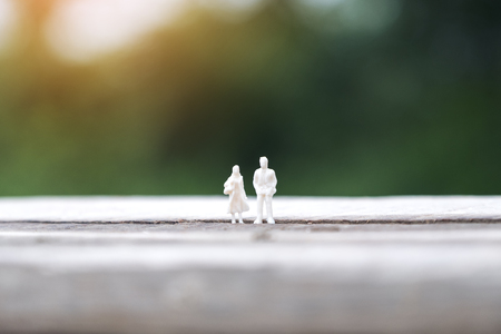 Closeup image of miniature figure model of a man and a woman standing together on wooden table with blur backgroundの写真素材
