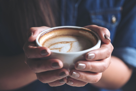 Closeup image of a woman holding a cup of coffee before drinking with feeling good and relaxed  in cafeの写真素材