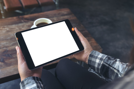 Mockup image of a woman holding black tablet pc with white blank screen with coffee cup on table backgroundの写真素材