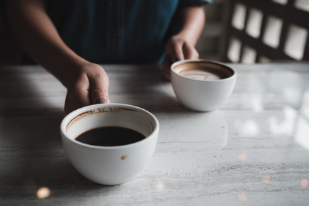 Closeup image of hands holding two white cups of hot coffee on table in cafeの写真素材