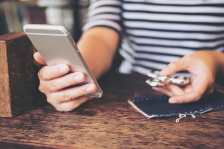 A woman holding smart phone while playing fidget spinner on vintage wooden tableの写真素材