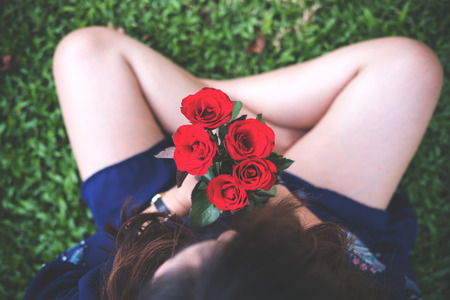 Top view image of woman sitting on green grass and holding red roses flowerの写真素材