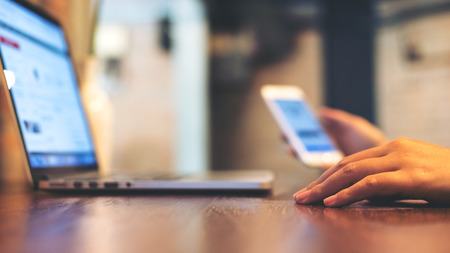 A business woman holding mobile phone while using laptop on wooden table in office