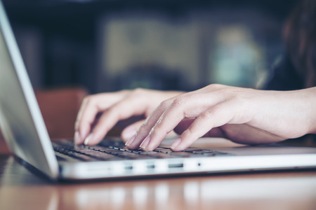 Closeup image of a business woman's hands working and typing on laptop keyboard on wooden table in...