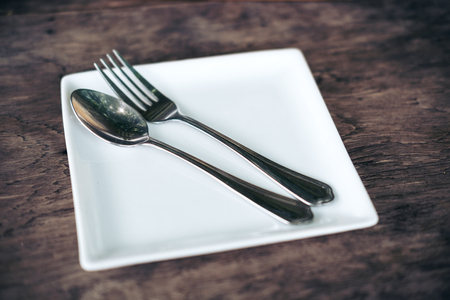 One set of spoon and fork in a white plate on vintage wooden table