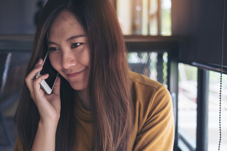A beautiful Asian woman holding and talking on smart phone in cafeの写真素材