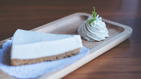 A piece of yogurt cheese pie and whipped cream in wooden plate on wooden table in bakery shop
