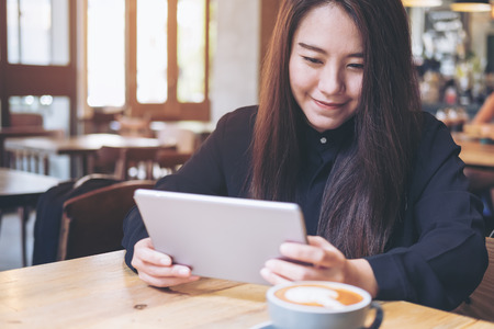 A beautiful Asian woman with smiley face using tablet in modern cafeの写真素材