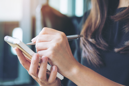 Closeup image of a woman writing and taking note on notebook in officeの写真素材