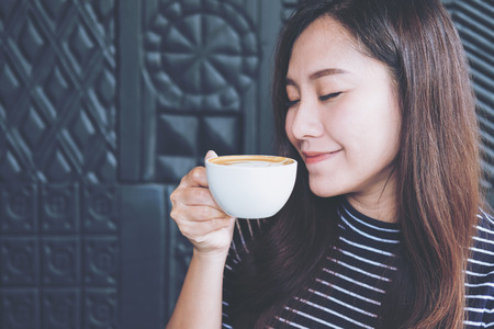Closeup image of beautiful Asian woman close her eyes smelling and drinking hot coffee with feeling good in cafeの写真素材