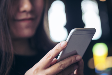 A beautiful Asian girl with smiley face looking and using smart phone in modern cafe with blur bokeh backgroundの写真素材