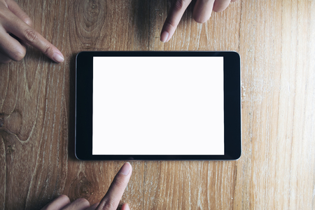 Three fingers of business man pointing at mockup of black tablet pc with blank white screen on vintage wooden table backgroundの写真素材