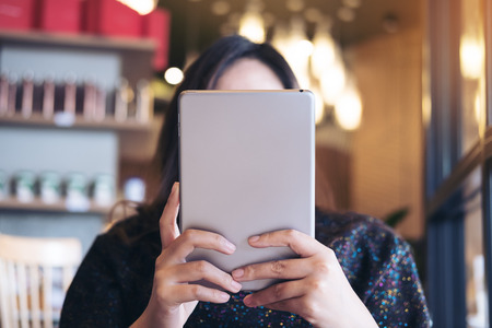 A woman sitting in cafe looking , using and holding tablet pc cover her face