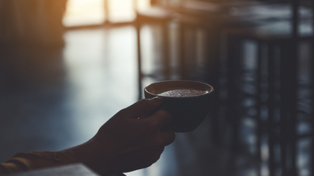 Closeup image of a hand holding a cup of coffee in cafeの写真素材