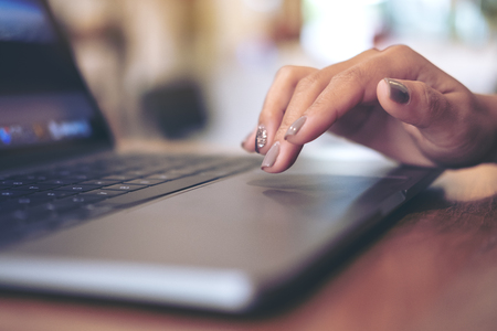 Closeup image of a woman's hands using and touching laptop keyboard on table