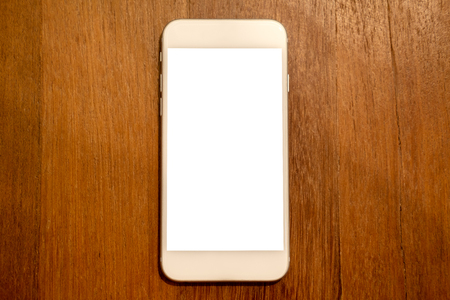 Top view mockup image of white mobile phone with blank desktop screen on wooden table backgroundの写真素材