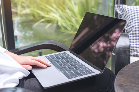 Mockup image of a woman using , touching and typing on laptop with blank white desktop screen while sitting on a chairの写真素材