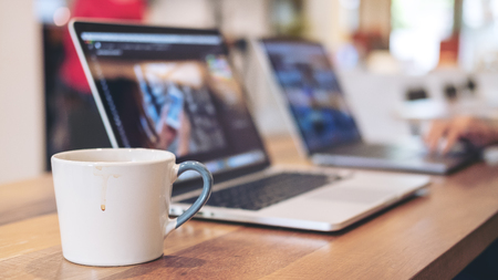 Closeup image of people working and typing on laptop keyboard with coffee cup on table in office