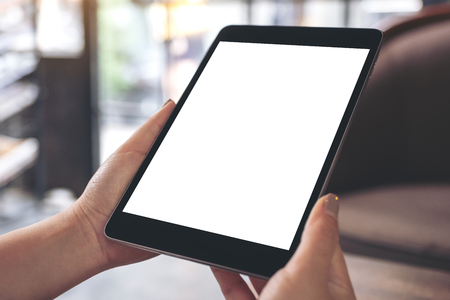 Mockup image of hands holding black tablet pc with white blank desktop screen in cafeの写真素材