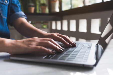 Closeup image of a woman's hands working and typing on laptop keyboard on tableの写真素材