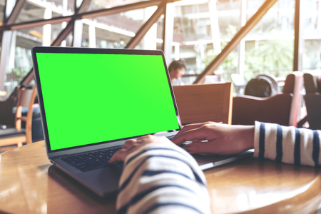 Mockup image of a woman using and typing laptop with blank desktop screen on wooden table in cafeの写真素材