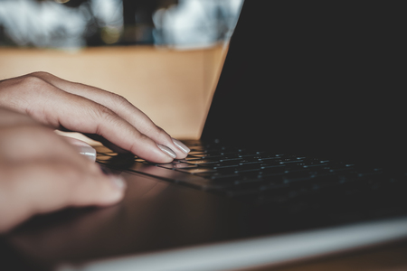 Closeup image of a woman's hands using and typing on laptop keyboard on tableの写真素材