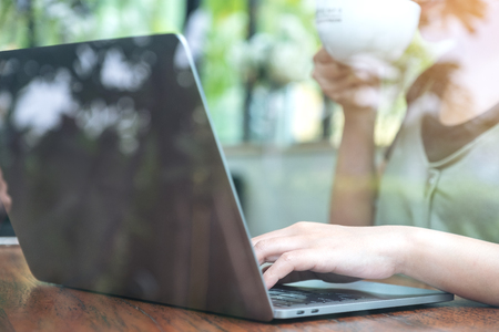Closeup image of a woman working and typing on laptop keyboard while drinking coffeeの写真素材