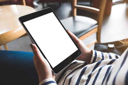 Mockup image of woman's hands holding black tablet pc with blank white desktop screen while sitting in cafeの写真素材