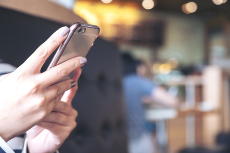 Closeup image of a woman's hands holding , using and looking at smart phone in cafe with blur backgroundの写真素材