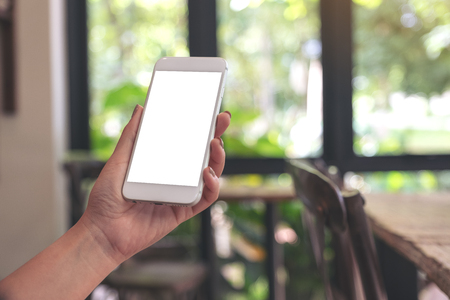 Mockup image of a woman holding and looking at a white smart phone with blank desktop screen with blur green nature backgroundの写真素材
