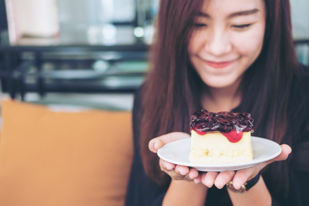 A beautiful asian woman holding  blueberry cheese cake  with feeling happy and good lifestyle in modern cafeの写真素材