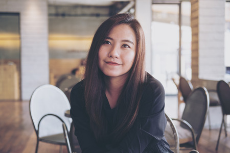 A beautiful Asian woman sitting in modern cafe with smiley face and feeling happyの写真素材