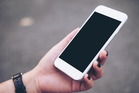 Mockup image of hand holding white mobile phone with blank black screen with blur gray color backgroundの写真素材