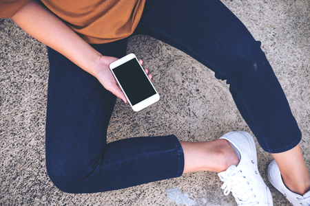 Mockup image of a woman sitting on the street and holding mobile phone with blank white screenの写真素材