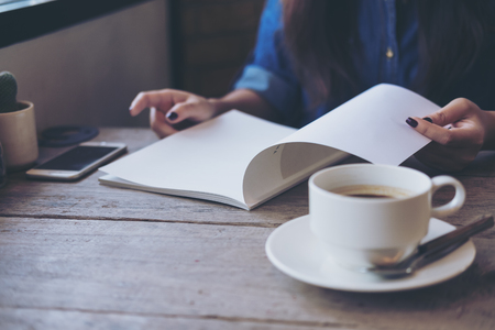 A woman opening and reading a book with coffee cup on wooden table in vintage cafeの写真素材
