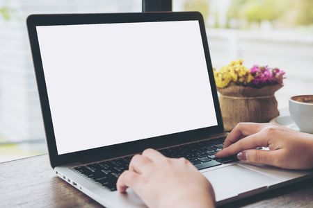 Mockup image of hands using laptop with blank white screen on vintage wooden table in cafeの写真素材