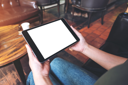 Mockup image of woman's hands holding black tablet pc with blank desktop screen while sitting in cafeの写真素材