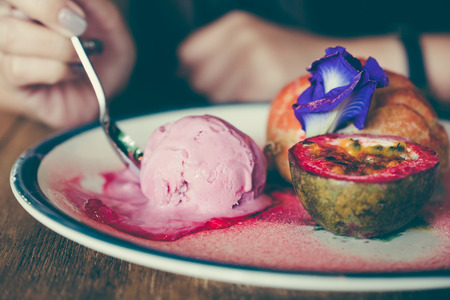 Closeup image of woman eating a dish of Choux cream , rose ice-cream and passion fruit with beautiful decorationの写真素材