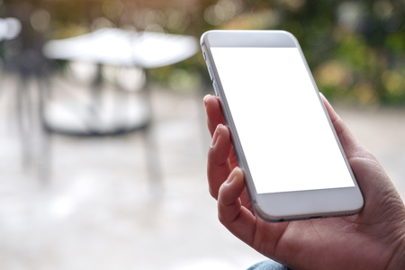 Mockup image of hands holding white mobile phone with blank desktop screen and blur backgroundの写真素材
