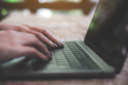 Closeup image of a business woman's hands working and typing on laptop keyboard on wooden table with blur backgroundの写真素材