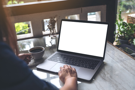 Mockup image of a woman using and typing on laptop with blank screen while drinking coffee in modern cafeの写真素材
