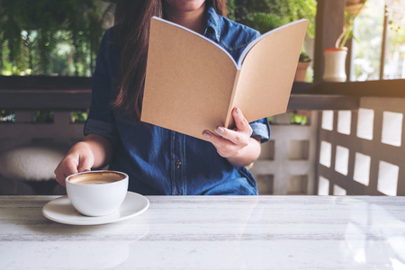 Closeup image of a beautiful asian woman reading a book while drinking coffee in modern cafeの写真素材