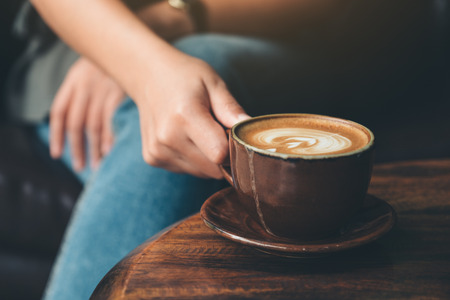 Closeup image of a woman holding  a cup coffee on vintage wooden table in cafeの写真素材