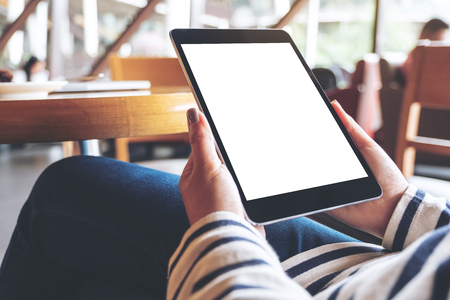 Mockup image of woman's hands holding black tablet pc with blank white desktop screen while sitting in cafeの写真素材