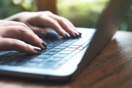 Closeup image of woman's hands working and typing on laptop keyboard on wooden table with green nature backgroundの写真素材