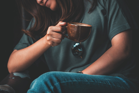 Closeup image of an Asian woman holding and drinking hot coffee with feeling relaxed in vintage cafeの写真素材