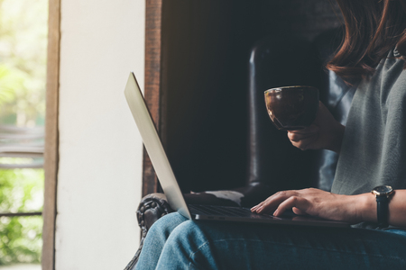 Closeup image of a woman working and typing on laptop keyboard while drinking coffeeの写真素材