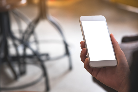 Mockup image of a hand holding white mobile phone with blank desktop screen in cafeの写真素材